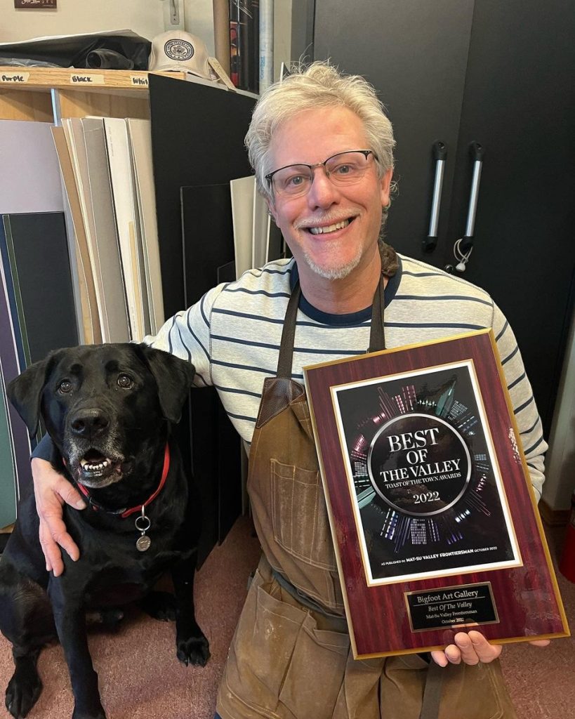 Image of the business owner and pet dog posing with the award plaque.